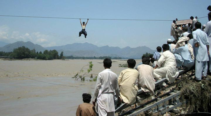 Пакистанцы наблюдают, как мужчина перебирается через реку по канату, с разрушенного моста в Чакдаре, Пакистан, 3 августа 2010 года.